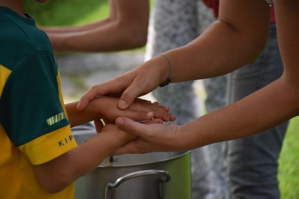 A caregiver assisting a child in handwashing outdoors, promoting hygiene and care.